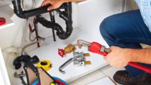 Plumber fixing under-sink drainage pipes using a red pipe wrench, professional service by Pro Speedy Plumbers.