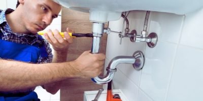 Plumber using a tool to repair sink drain pipes in Kensington W8.